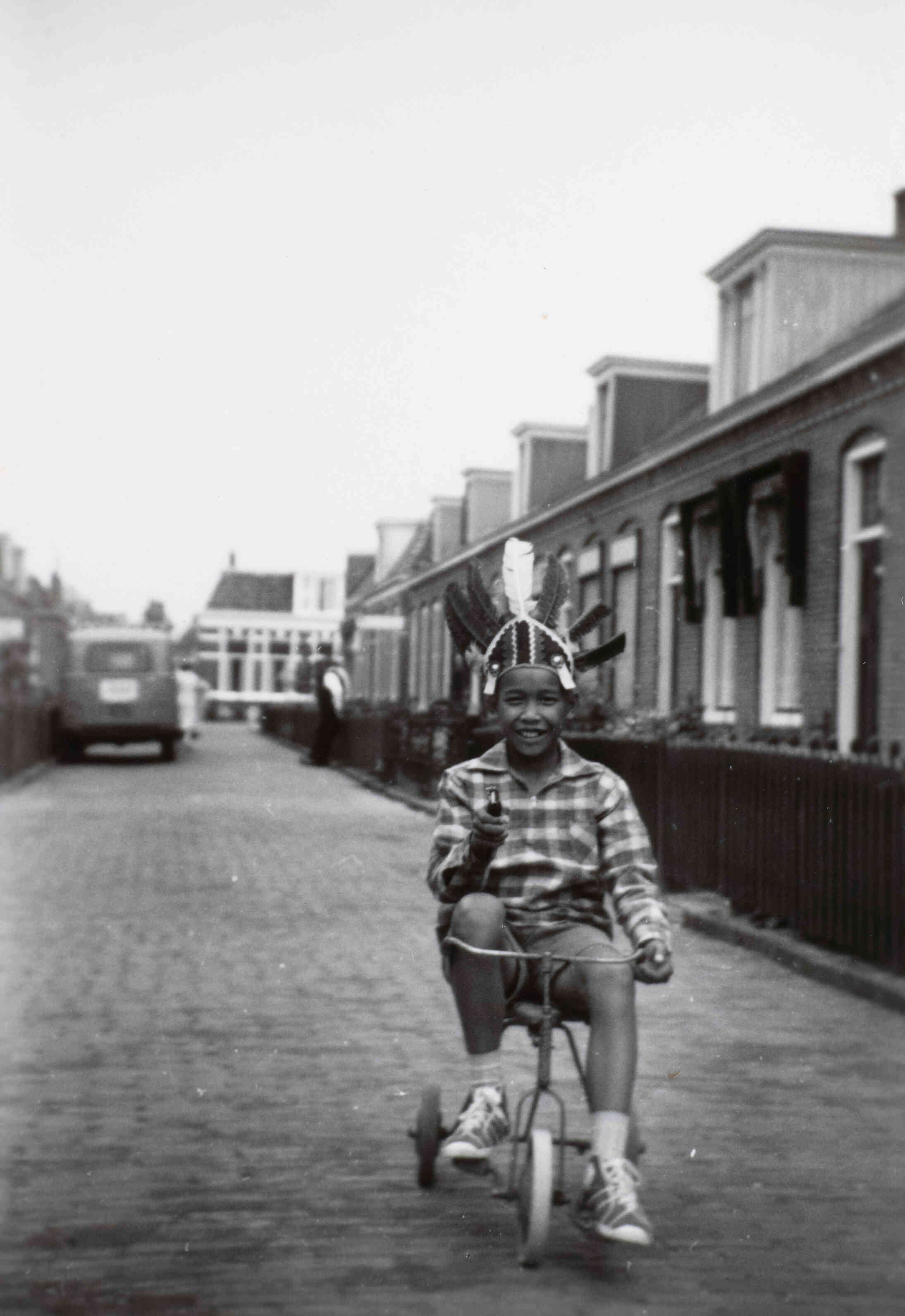 Ambonees kind met indianentooi, op driewieler in de Paulus Moreelsestraat, te Huizum, Friesland